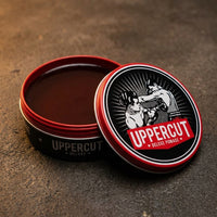Uppercut Deluxe Pomade - open blik met glanzende bruine inhoud op beton