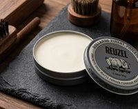 Reuzel Concrete Hold Matte Pomade - open blik met matte inhoud, borstels op leisteen