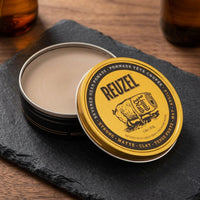 Reuzel x Liquid Death Clay Pomade - open blik met klei op leisteen bij amberflessen