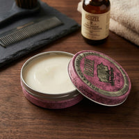 Reuzel Pink Pomade Grease - open blik met kam en flesje op houten tafel