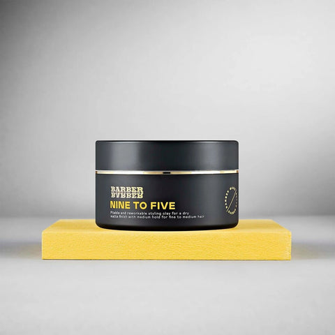 BARBER BARBER Nine To Five Medium Hold Styling Clay 100g - zwart potje op geel blok, grijze studio