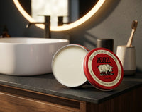 Reuzel Red Pomade - open blik met witte inhoud, deksel ertegenaan in badkamer