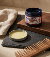 Blue Magic Pressing Oil - öppen burk på skiffer med träkam, den gula oljan synlig